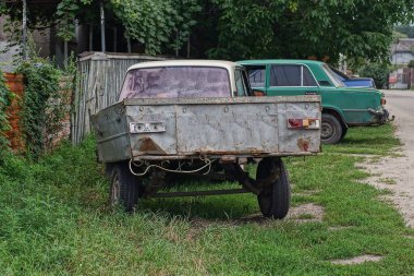 an one old gray metal trailer stands on green grass near a wooden fence on the street