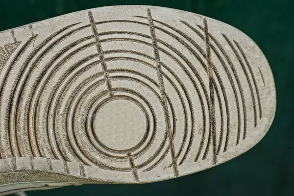 white gray rubber sole of one dirty boot with a pattern on a green background