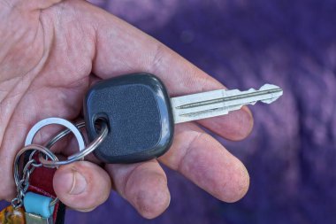 hand holding one car ignition key on purple background