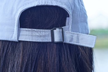 white baseball cap with a latch and a harness on the head of a girl with long black hair at the back of her head on the street