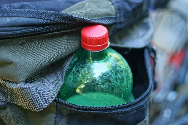 one green plastic bottle with a red cork in the pocket of a gray bag on the street