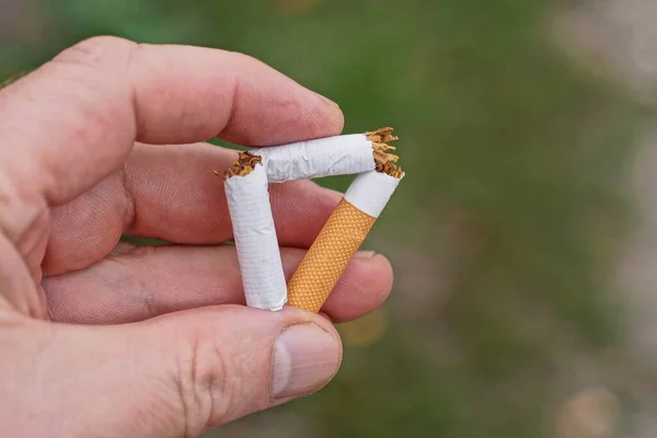 one broken white cigarette with a brown filter lies on the palm of his hand