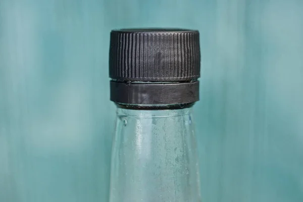 part of glass bottle with soy sauce with closed  black plastic cap on green background