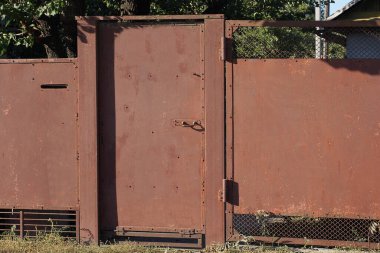 one brown iron closed door on a metal fence wall on a rural street