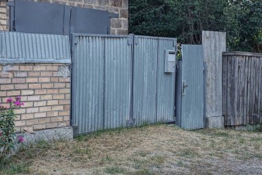 one gray metal gate and a closed door on a brown brick wall of a fence in a rural street