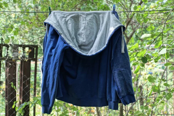 one blue jacket made of fabric with a white hood hangs on a wire in the street among green vegetation