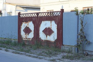 Eski bir kırsal demir, kahverengi beyaz kapı. Sokakta yeşil çimlerde metal, gri bir çit duvarında deseni var.