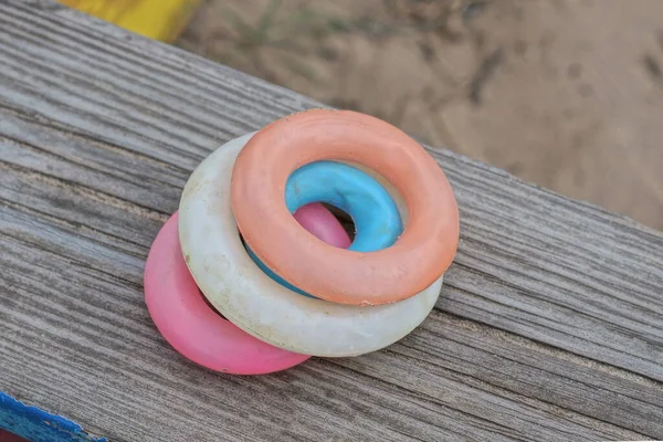 round colored plastic toy rings lie on a gray wooden board in the street