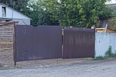 one big closed brown gate and gray concrete fence on a rural street