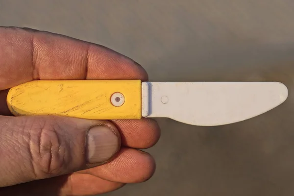 Ręka Trzyma Biały Żółty Plastikowy Mały Nóż Zabawki Szarym Tle — Zdjęcie stockowe