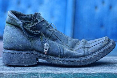 Eski, kirli siyah bir ayakkabı, gri bir masada mavi bir arka planda duruyor.