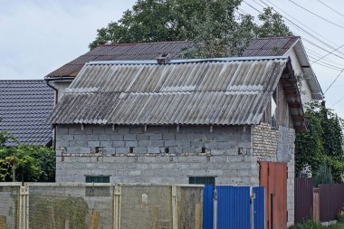Bir tuğladan özel garaj, kahverengi demir kapılı, gri tahta çatılı, dışarıda sarı ve mavi metal çitlere karşı.