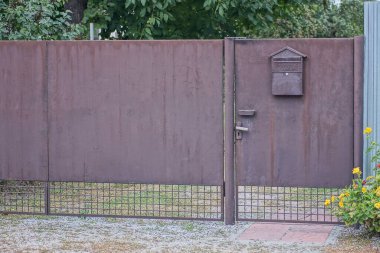 Kapalı kahverengi metal kapı, posta kutusu ve kırsal bir sokakta demir kapı.