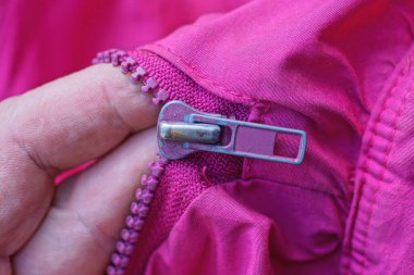 Eldeki parmaklar, ceketteki pembe kumaşta metal bir fermuar tutuyor.