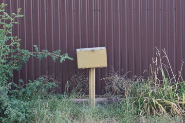 Yeşil çimenlikteki bir direkte elektrik kabloları için bir sarı metal kutu ve dışarıdaki kahverengi demir çit duvarının yanında bitki örtüsü.