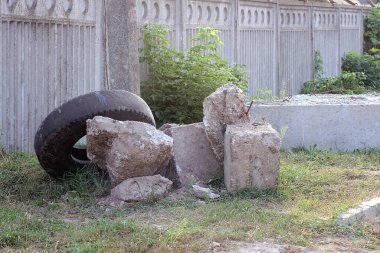 Bir yığın gri beton blok ve yeşil çimlerde siyah bir araba lastiği çitin yanında.