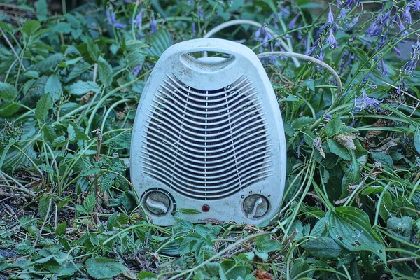 one white mobile dirty fan stands  on green plant  and the ground in nature