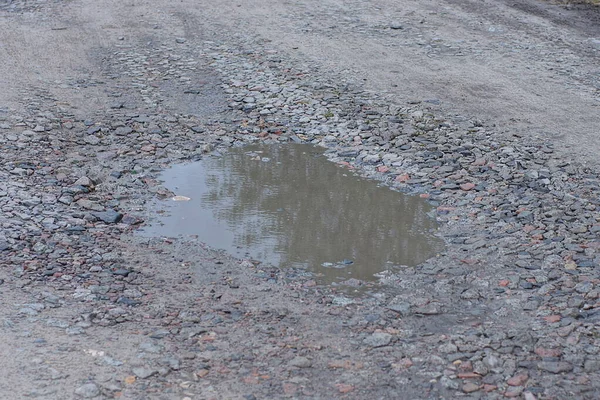 one big puddle with dirty water on the gray ground of the road outside