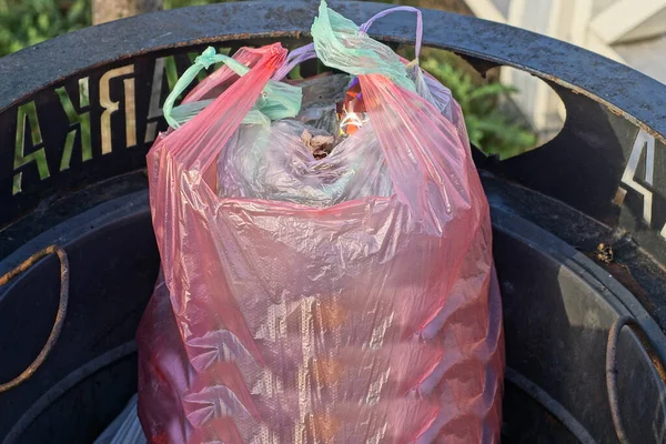 a pink plastic bag full of garbage lies in a black metal urn on the street