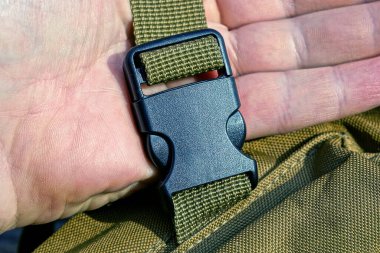 Sırt çantasının yeşil kayışında siyah plastik bir karabina tutuyor.