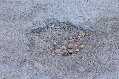 Gri asfaltta büyük bir çukur ve yolda da toprak.