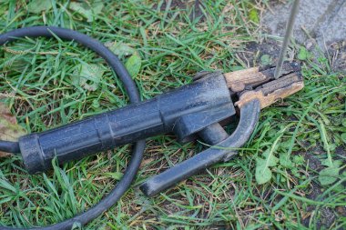 Testisli kaynak makinesinin bir parçası ve siyah elektrik kablosu üzerinde bir elektrot sokaktaki yeşil çimlerin üzerinde yatıyor.