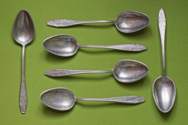 Altı eski alüminyum kaşıktan yapılmış tabaklar yeşil bir masada yatıyor.