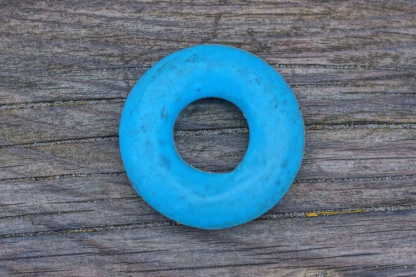 one blue round plastic toy ring lies on a gray wooden board in the street