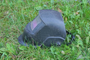 Elektrikli kaynakçı için bir siyah metal maske sokaktaki yeşil çimlerde yatıyor.