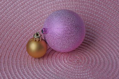 iki cam mor ve kahverengi Noel topları pembe bir masanın üzerinde yatıyor.