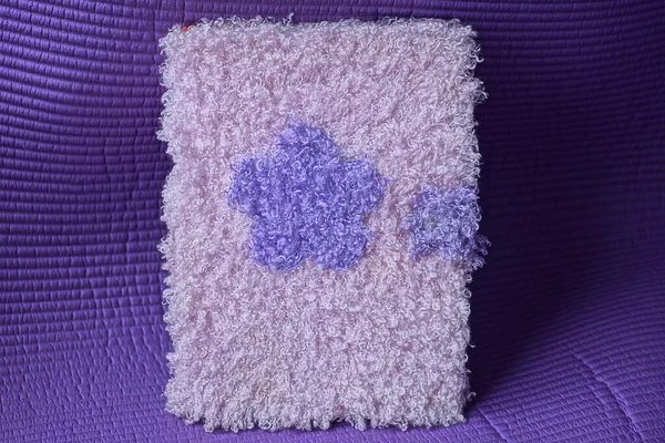one rectangular notebook with a woolen colored fabric cover stands on a purple table