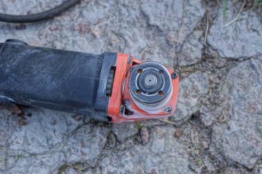 Siyah kırmızı bir öğütücüden alınan tek bir elektrikli aletin parçası sokaktaki gri betonun üzerinde yatıyor.