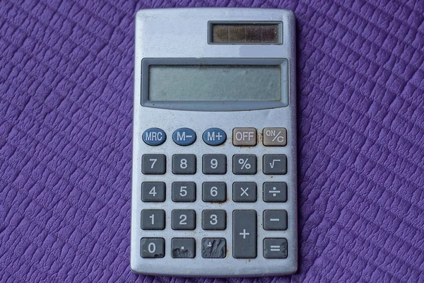 one old gray electronic calculator lies on a purple table