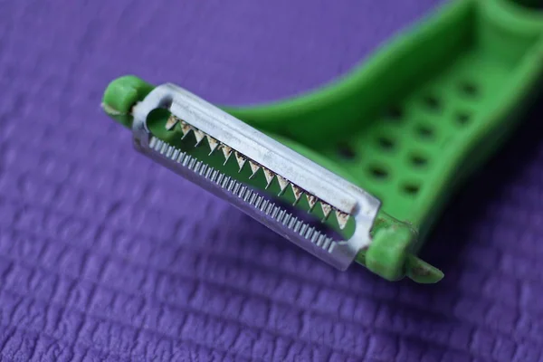 歯を持つ金属製の刃を持つプラスチック製の緑の皮1枚が紫色のテーブルの上にあり — ストック写真