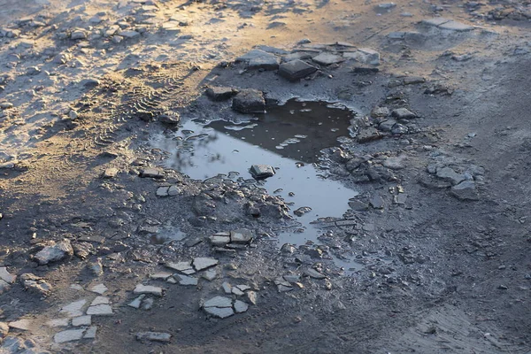 one puddle with dirty water on the gray ground of a rural road in the street