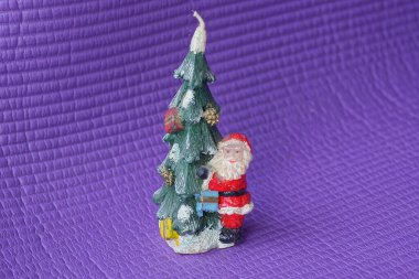 Küçük plastik bir Noel Baba oyuncağı mor bir masada duruyor.