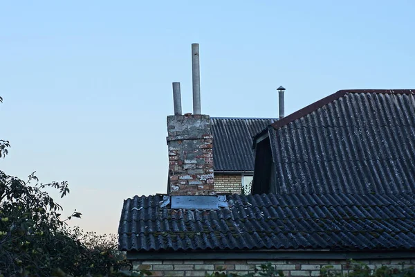 old chimney on a gray slate roof of a rural house against a blue sky