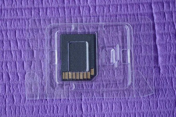 透明プラスチックパッケージの1つの小さな黒いリムーバブル記憶装置は紫色のテーブルの上にあります — ストック写真