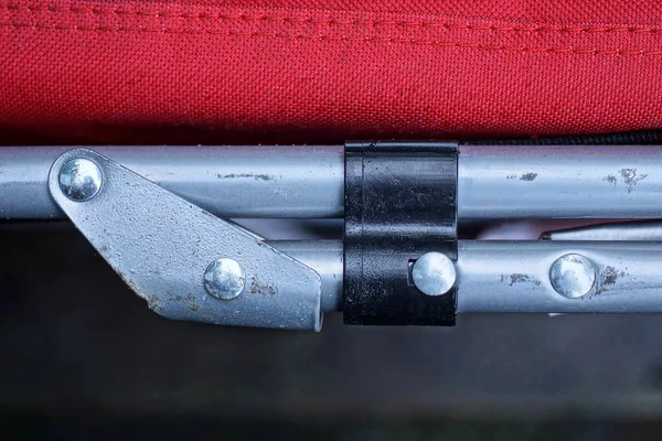 Alüminyum gri tüplerden yapılmış bir yapının parçası. Bağlayıcı ve cıvatalı kırmızı kumaşlı bir arabada.