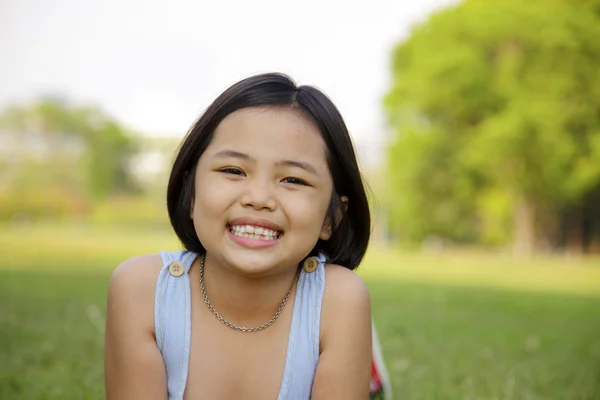 Asiatiska liten flicka slappna av och ler glatt i parken — Stockfoto