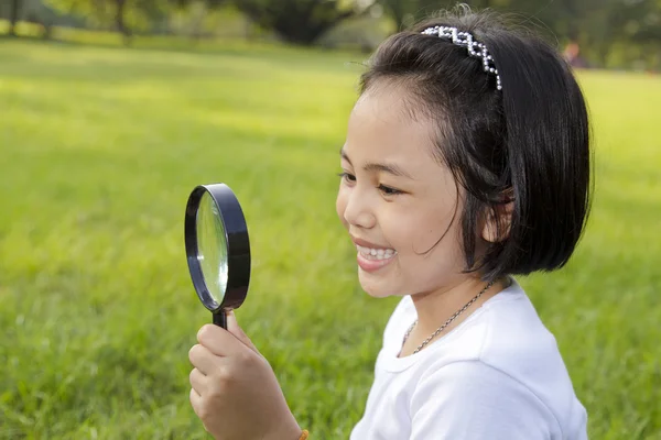 Asiatische kleine Mädchen hält ein Vergrößerungsglas im Freien — Stockfoto