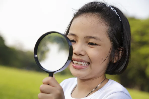 Asian little girl holding a magnifying glass in outdoor — Stock Photo, Image