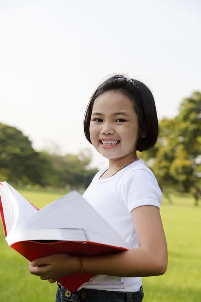 Asiatisches kleines Mädchen öffnet ein Buch im Park — Stockfoto