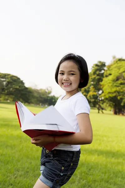 Asiatiska liten flicka öppnar du en bok i parken — Stockfoto