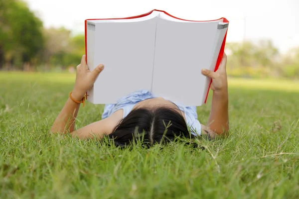 Asiatisches kleines Mädchen liest Buch im Park — Stockfoto