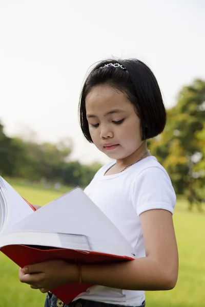 Asiatisches kleines Mädchen öffnet ein Buch im Park — Stockfoto