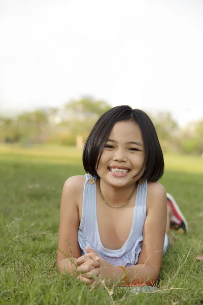 Asiatiska liten flicka slappna av och ler glatt i parken — Stockfoto