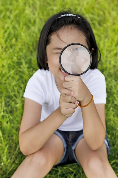 Asian dziewczynka gospodarstwa szkło powiększające w odkrytym — Zdjęcie stockowe