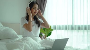Kulaklıklı Asyalı kadın sabahları yatakta müzik dinliyor.
