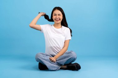 Güzel kız mavi bir arka planda oturuyor, gülümsüyor, mutlu, rahatlatıcı, heyecanlı, eğleniyor..